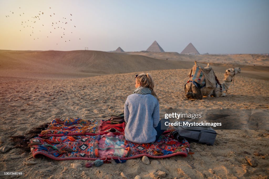Frau beobachtet Sonnenuntergang an den Pyramiden von Gizeh, sie blickt über die Sahara