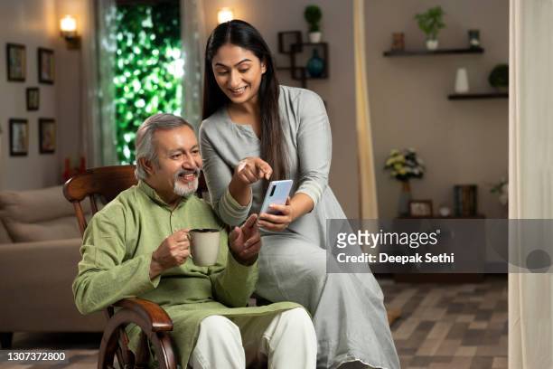 portrait of a young woman and her mature father sitting on rocking chair at home. she is showing something in mobile phone :- stock photo - portable information device stock pictures, royalty-free photos & images