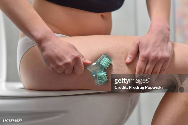 young woman using skin roller on her legs in bathroom - cellulite stock-fotos und bilder
