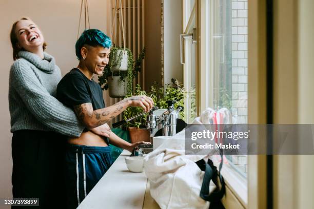 happy woman embracing while female roommate making coffee on kitchen counter - coffee maker stock-fotos und bilder