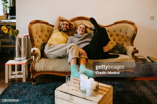 smiling male and female roommates sitting on sofa at home - room mates male stock-fotos und bilder