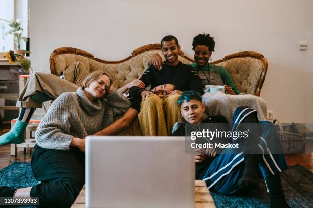 smiling male and female watching movie on laptop in living room - young people looking at camera foto e immagini stock