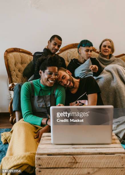male and female friends laughing while watching movie on laptop at home - download photos et images de collection