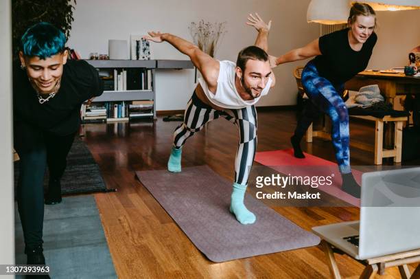 smiling male and female learning online yoga tutorial through laptop in living room - net sports equipment foto e immagini stock