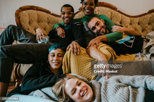 portrait of smiling male and female friends relaxing in living room - menschengruppe stock-fotos und bilder