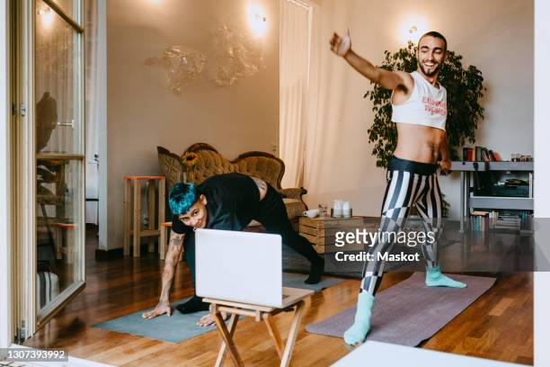 active male and female friends practicing yoga tutorial online in living room - yoga germany stockfoto's en -beelden