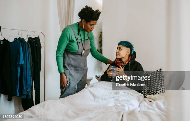 female roommate taking care of sick woman at home - krankenbett gespräch stock-fotos und bilder