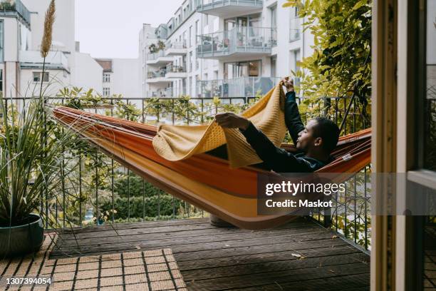 young man lying in hammock at back yard - hammock stock-fotos und bilder