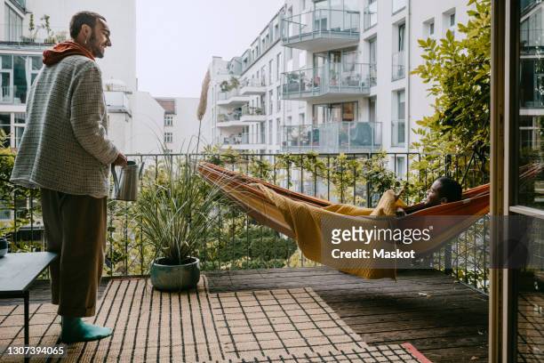 young man looking at male friend lying in hammock at back yard - garden hammock stock pictures, royalty-free photos & images