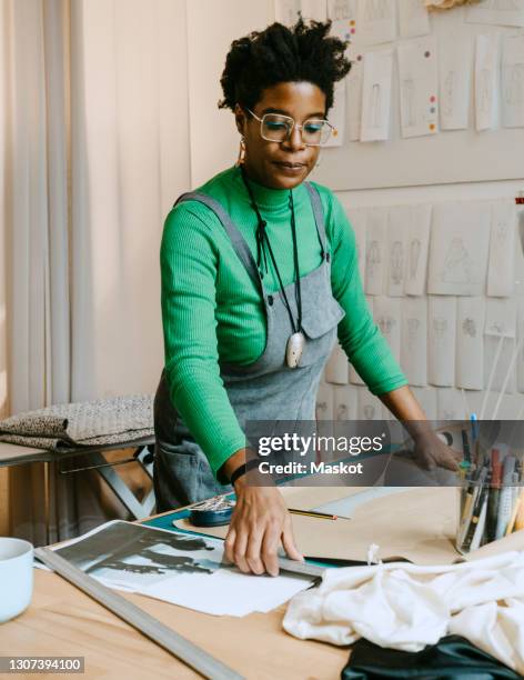 mid adult woman concentrating while doing craft at table in living room - craft table stock pictures, royalty-free photos & images