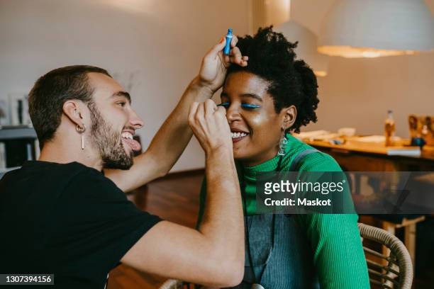 smiling man applying blue eyeliner to female friend at home - trucco per il viso foto e immagini stock
