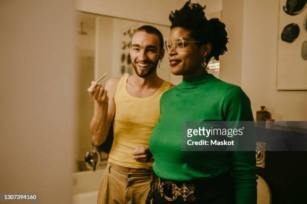 smiling man with make-up brush standing by female friend in bathroom - bad relationship stock-fotos und bilder