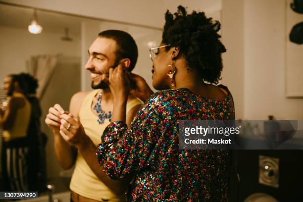 female friend helping smiling male roommate while wearing earring in bathroom - bad relationship stock-fotos und bilder