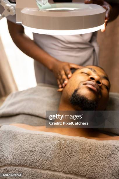 hombre recibe tratamiento facial en spa de belleza - black massage therapist fotografías e imágenes de stock