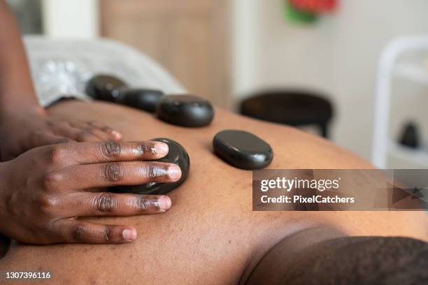 mujer de primer plano masajea a hombre con rocas calientes - black massage therapist fotografías e imágenes de stock