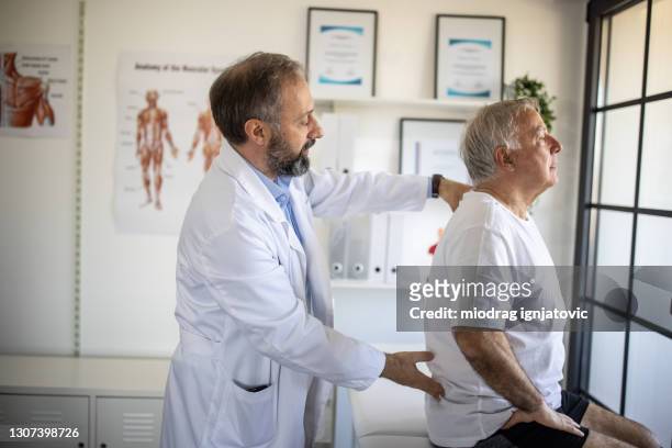 医師のオフィスでシニア患者の背中の怪我を調べる理学療法士 - 腰痛 ストックフォトと画像