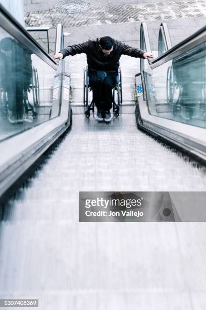 handicapped man starting up the escalator with his wheelchair. - southern european descent stockfoto's en -beelden