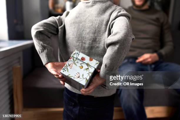 boy hiding gift for his father behind the back - surprise gift foto e immagini stock