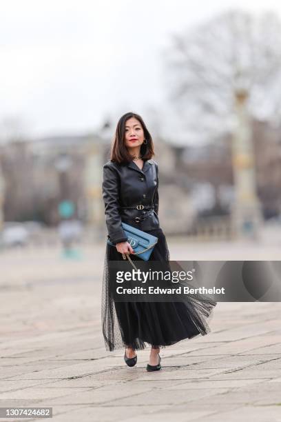 May Berthelot @may.berthelot wears earrings, a golden Dior necklace, a black leather jacket from Dior, a Dior belt, a blue Dior bag, a black mesh...