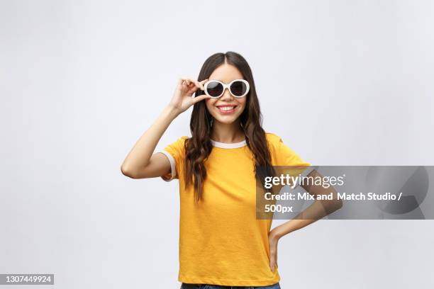 portrait of smiling young woman wearing sunglasses while standing against white background - yellow sunglasses stock pictures, royalty-free photos & images