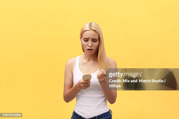 young woman using mobile phone while standing against yellow background - cheveux secs photos et images de collection