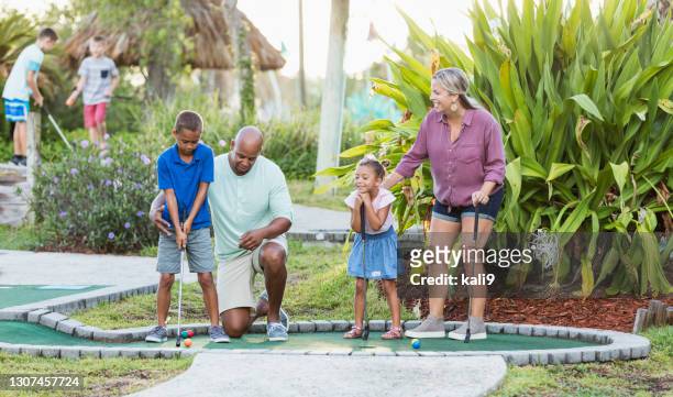 interracial family, two children playing miniature golf - golf girls stock pictures, royalty-free photos & images