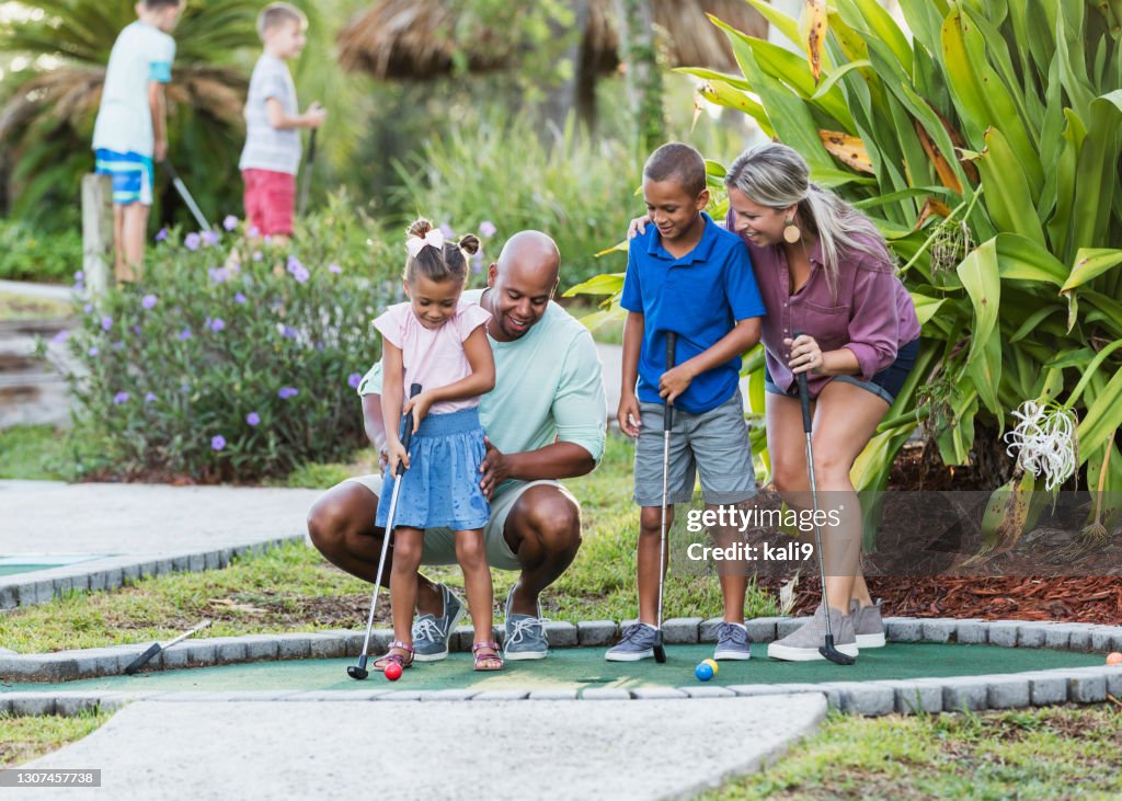 Interracial family, two children playing miniature golf