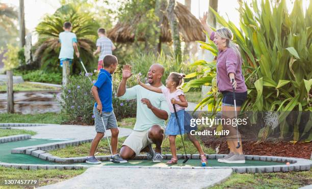 interracial family, two children playing miniature golf - putt stock pictures, royalty-free photos & images