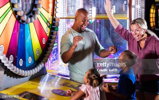 interracial familie, zwei kinder gewinnen ein arcade-spiel - spinnrad stock-fotos und bilder