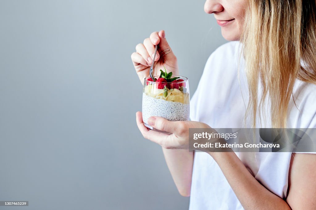 Close-up of a young woman in a white shirt with chia seed pudding with berries and fruit