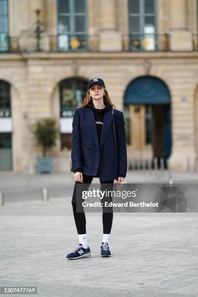 Olesya Senchenko wears a NY blue cap hat, a black hoodie sweater, a navy blue blazer jacket, a black leather quilted Chanel bag, black leggings, Nike...