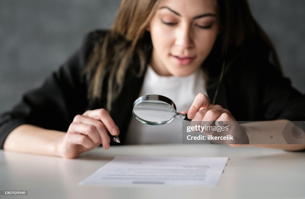 署名前に虫眼鏡を使用して慎重に法的文書を読むビジネスウーマン