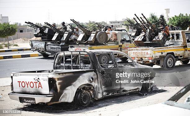 Heavily-armed gun trucks reverse slowly up the main street, past a burnt out vehicle, into the west of Sirte as rebels advance on the town on October...
