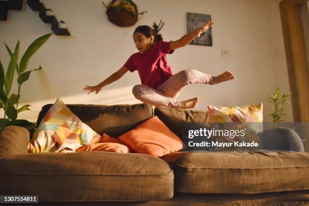 girl jumping on sofa at home - playing sofa stockfoto's en -beelden