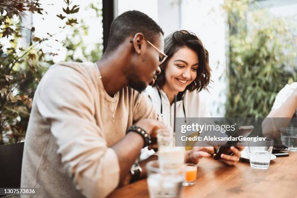 gemengd racepaar geniet van verfrissingen terwijl ze op zoek zijn naar producten om online op smartphone te kopen - coffee break party stockfoto's en -beelden