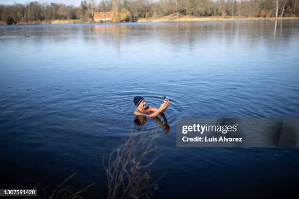 senior man in freezing cold lake taking selfie - eis baden stock-fotos und bilder