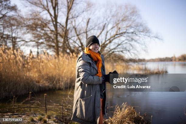 mature woman in warm clothes standing by the lake in forest - deutschland wald winter stock-fotos und bilder