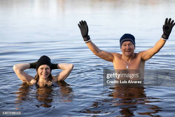 mature couple enjoying swimming in icy cold water lake - eis baden stock-fotos und bilder