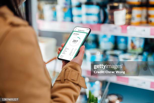 young woman checking nutrition and calories intake on smartphone while shopping in supermarket - app store stockfoto's en -beelden