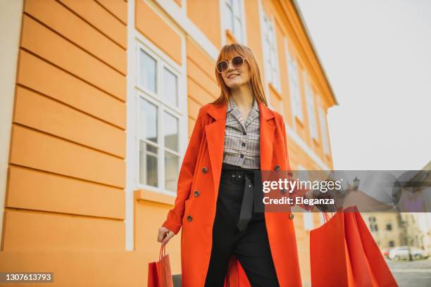retrato de la pelirroja en abrigo moderno con bolsas rojas de compras en la ciudad - fashion model bag fotografías e imágenes de stock