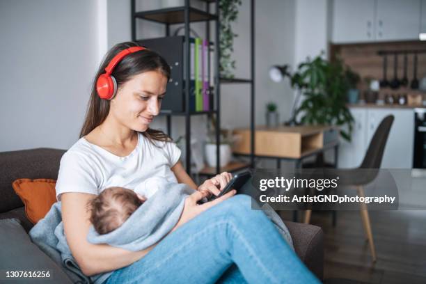 young mother relaxing at home while holding her sleeping baby. - mother media call stock pictures, royalty-free photos & images