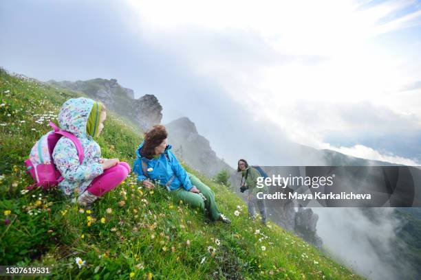 three generation family resting in beautiful meadow with flowers while hiking in mountains covered with mist - plovdiv stock pictures, royalty-free photos & images