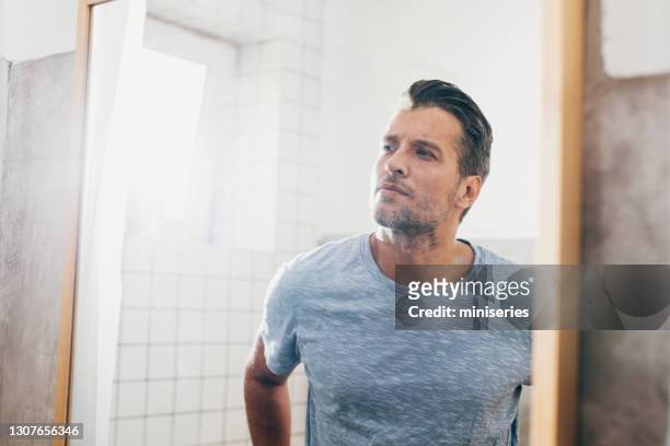 handsome young man checking his beard in a bathroom mirror - aftershave stock pictures, royalty-free photos & images