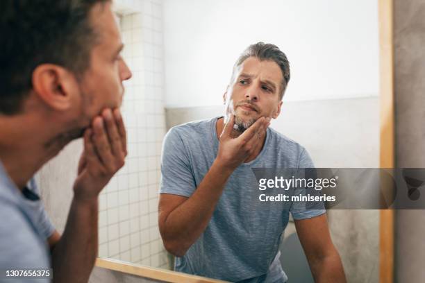 bel giovane che controlla la barba in uno specchio del bagno - shaving foto e immagini stock