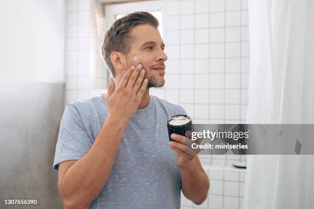 joven guapo aplicando crema facial después de un afeitado por la mañana - hombre crema facial fotografías e imágenes de stock