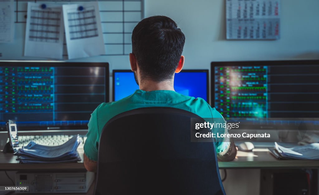 Back view of a nurse, checking on patients from monitors.