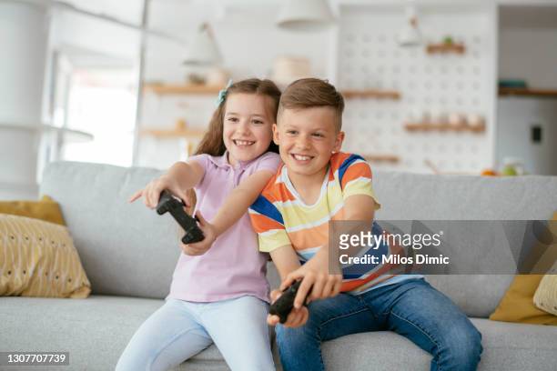 jonge broer en zuster die pret hebben terwijl het spelen van videospelletjes in woonkamer stockfoto - child playing in room stockfoto's en -beelden