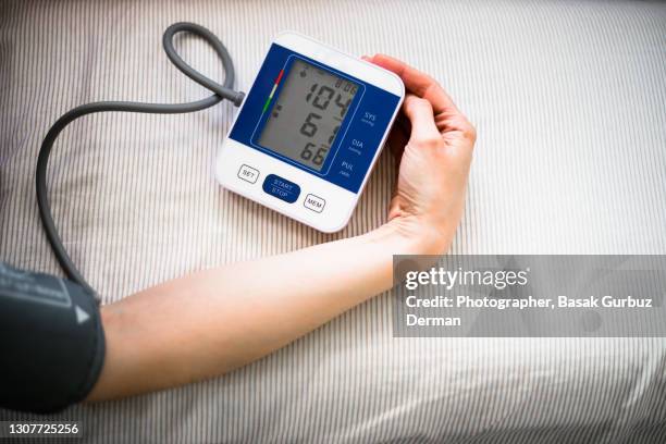 woman checking blood pressure using a digital automatic blood pressure monitor - high blood pressure stock pictures, royalty-free photos & images