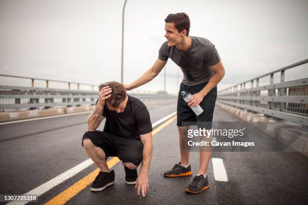supportive male athlete helping friend trying to rehydrate durin - heat exhaustion stock pictures, royalty-free photos & images
