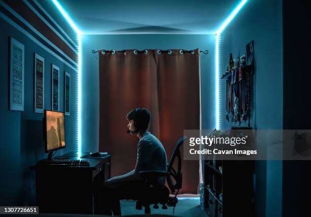 teenage boy playing video game at desk in room with neon led lighting. - computer gaming stock pictures, royalty-free photos & images
